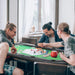 Friends playing a board game on a 10-player green felt folding poker table with cup holders