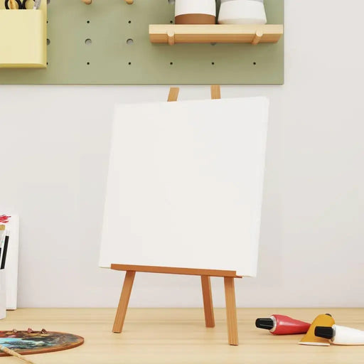 Blank stretched canvas on wooden easel for painting, art supplies and paint tubes nearby