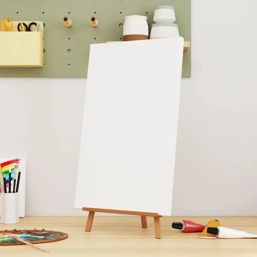Blank stretched canvas on mini easel with painting supplies in art studio workspace