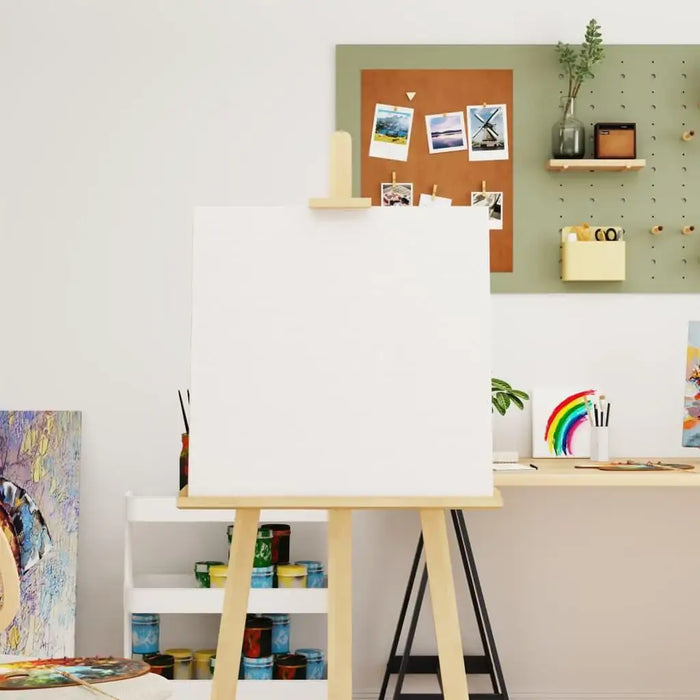 Blank stretched canvas on wooden easel in artist studio, painting supplies and decor in background