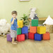 Toddler playing with colorful soft foam activity blocks in a playroom with toys and plants