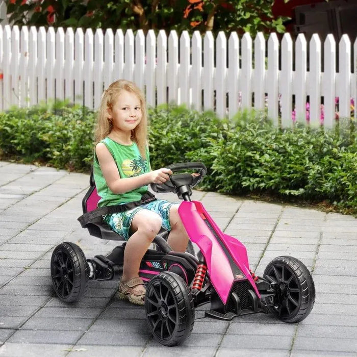 Child riding pink 12V electric go-kart on paved path by white picket fence outdoors