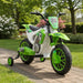Green and white toy dirt bike with training wheels in a front garden setting surrounded by plants