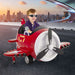 Smiling boy rides red 12V kids electric airplane toy with joysticks on city road at sunset