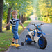 Child with 12V blue kids electric ride-on motorbike on outdoor path, trees in background