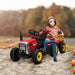 Child on red 12V electric ride-on tractor with detachable trailer in a pumpkin field
