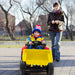 Child in a toy dump truck being pushed by an adult on a sidewalk.