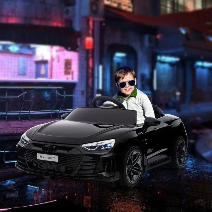 Smiling child in sunglasses driving black 12V Audi RS e-tron GT kids ride-on car with LED lights