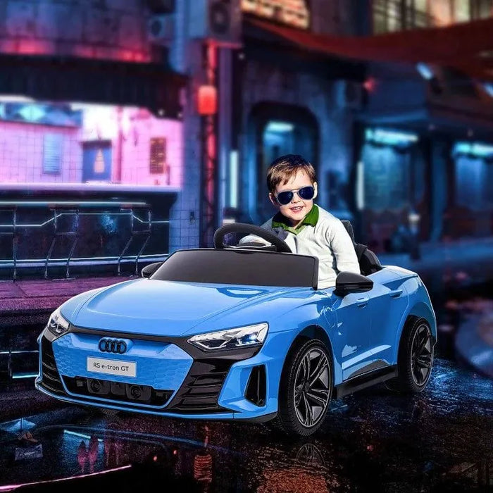 Child driving blue 12V Audi RS e-tron GT kids ride-on car with sunglasses in urban setting