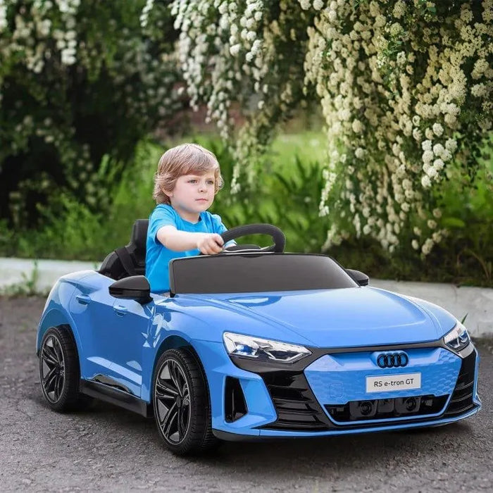 Child driving blue Audi RS e-tron GT kids ride-on car outdoors near flowering bushes