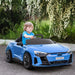 Child driving blue Audi RS e-tron GT kids ride-on car outdoors near flowering bushes