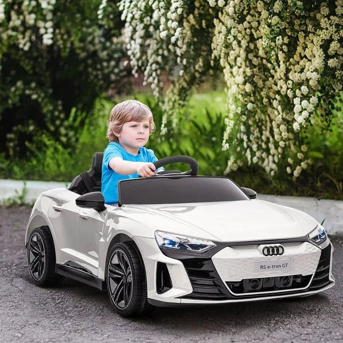 Child driving white licensed Audi RS e-tron GT kids ride on car outdoors under flowering trees