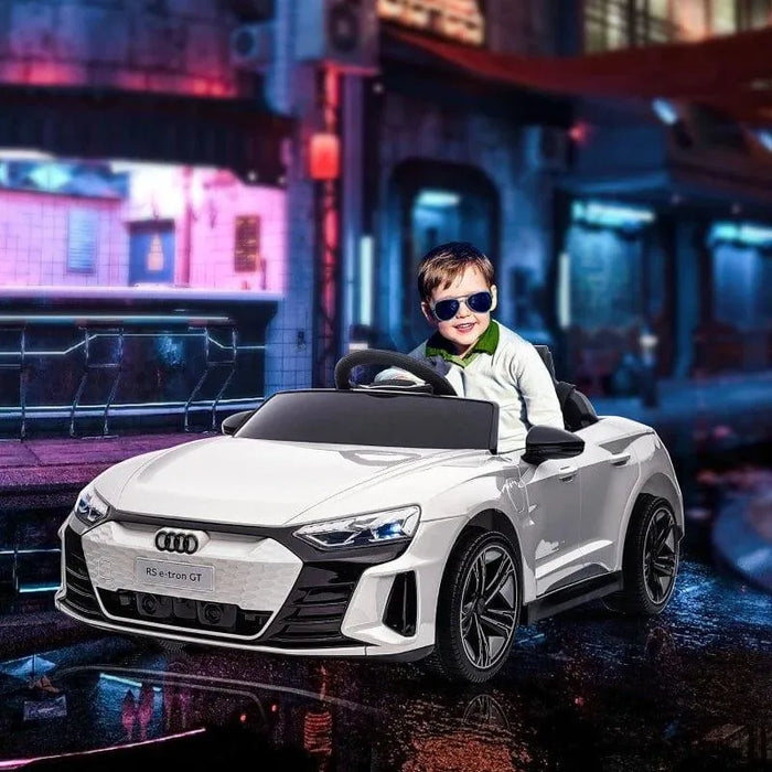 Child in sunglasses driving white Audi RS e-tron GT kids ride-on car with city lights background