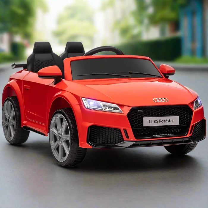 Red Audi TT RS kids electric ride-on car with lights on, shown outdoors on pavement.
