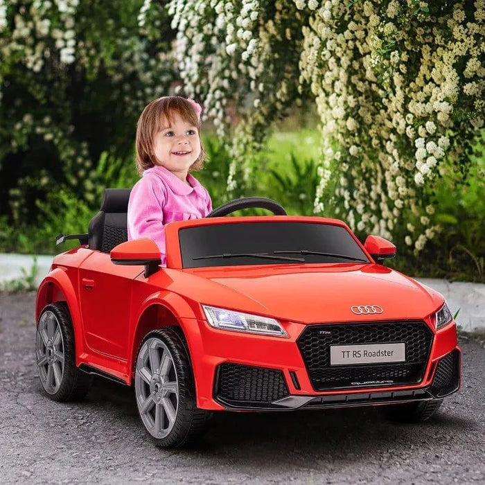Child driving red 12V Audi TT RS kids electric ride-on car outdoors with flowers