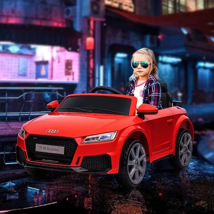 Child wearing sunglasses driving red Audi TT RS electric kids ride-on car in city setting