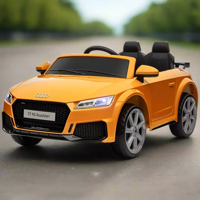 Yellow 12V Audi TT RS kids ride on car with headlights on, parked outdoors on road