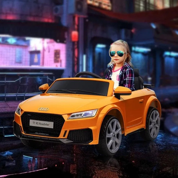 Child in yellow 12V Audi TT RS ride-on car with headlights, remote, city background