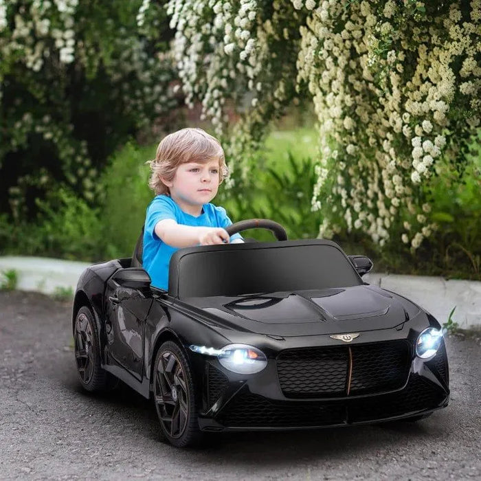 Boy riding black Bentley Bacalar kids electric ride-on car outdoors with butterfly doors