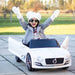 Child riding white 12V Bentley kids electric ride-on car outdoors with open doors