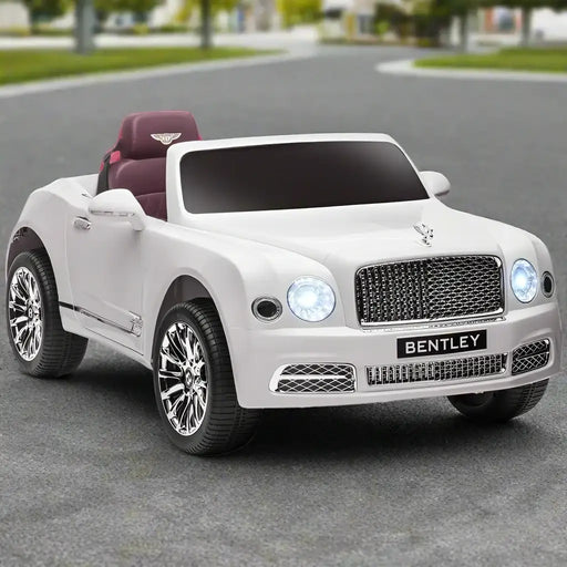 White 12V Bentley Mulsanne kids ride on car with chrome wheels, headlights on, outdoors.