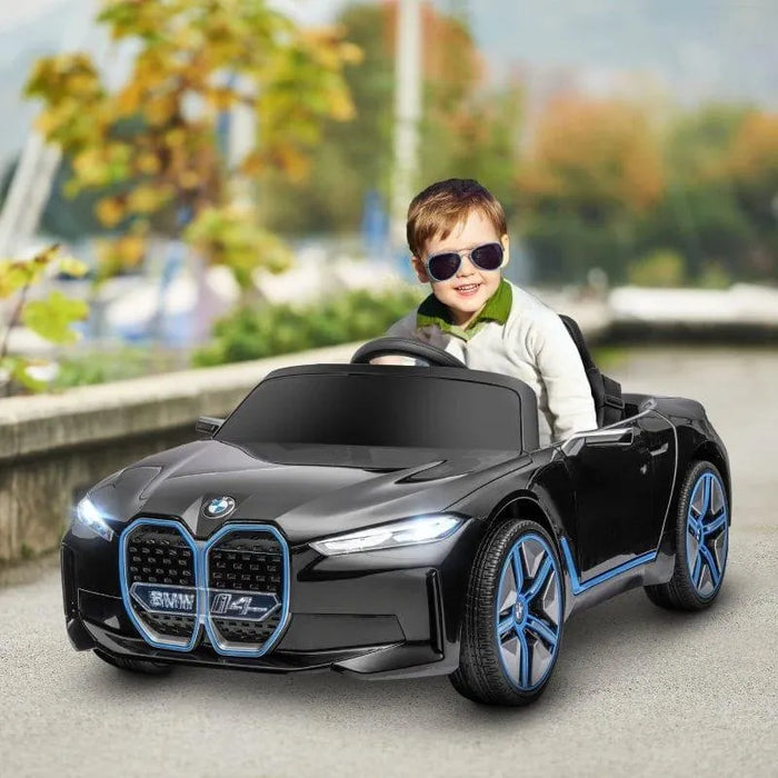Child in sunglasses driving black 12V BMW i4 kids electric ride-on car outdoors