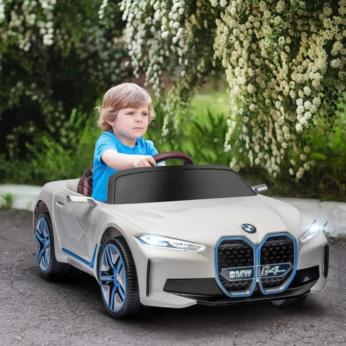 Child driving a white 12V BMW i4 kids ride on car outdoors with greenery and flowers