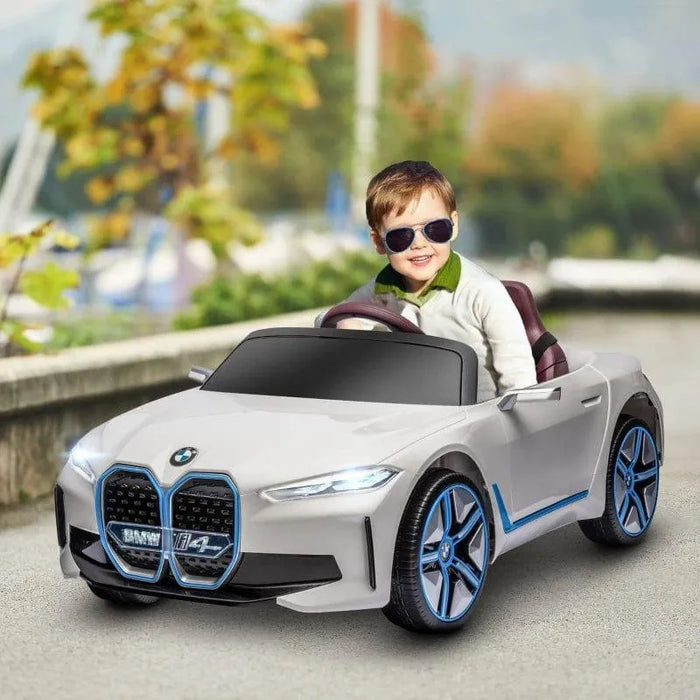 Child driving a white BMW i4 kids ride-on car with blue rims and sunglasses outdoors