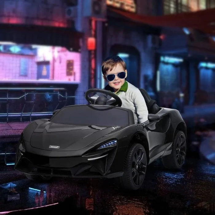 Child in sunglasses driving black 12V McLaren kids electric ride-on car at night