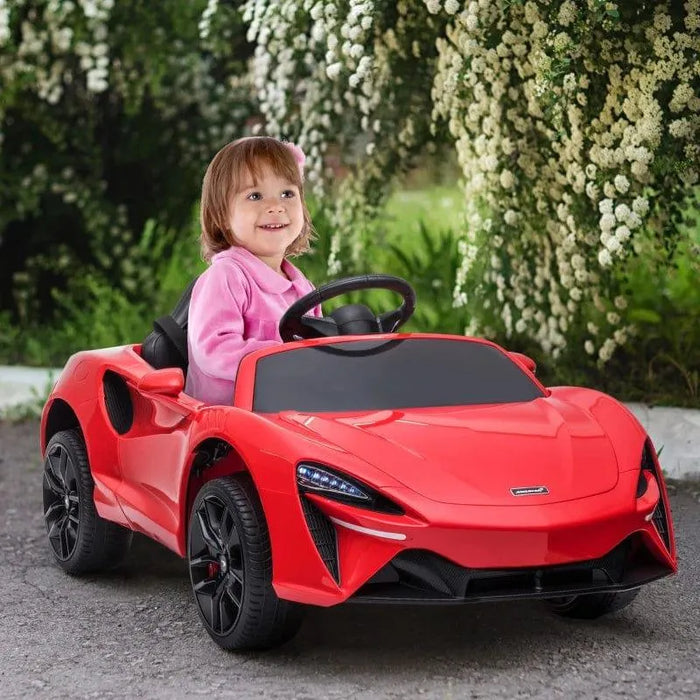 Child in red 12V McLaren kids ride-on car outdoors, smiling, surrounded by greenery