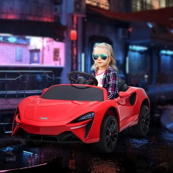 Little girl in sunglasses driving red 12V licensed McLaren kids ride-on car, city background