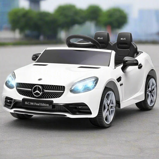 White Mercedes-Benz SLC kids electric ride-on car with LED headlights on gray pavement