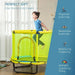 Child jumping on yellow and blue indoor kids trampoline with safety net in bright room