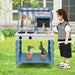 Child playing at blue double-sided mud kitchen with fabric canopy and toy accessories outdoors