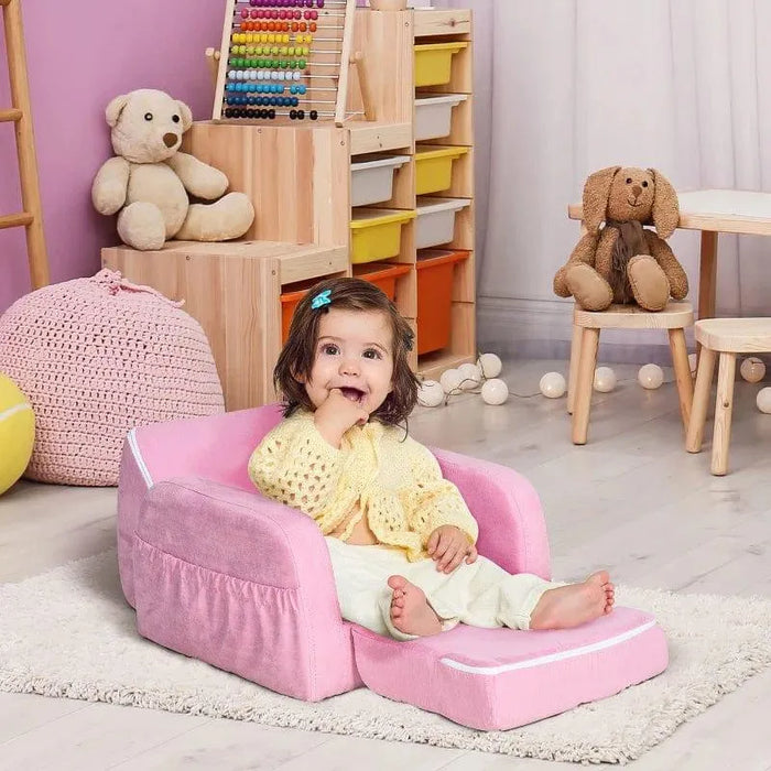 Toddler sitting on pink 2-in-1 kids chair convertible armchair sofa bed in playroom