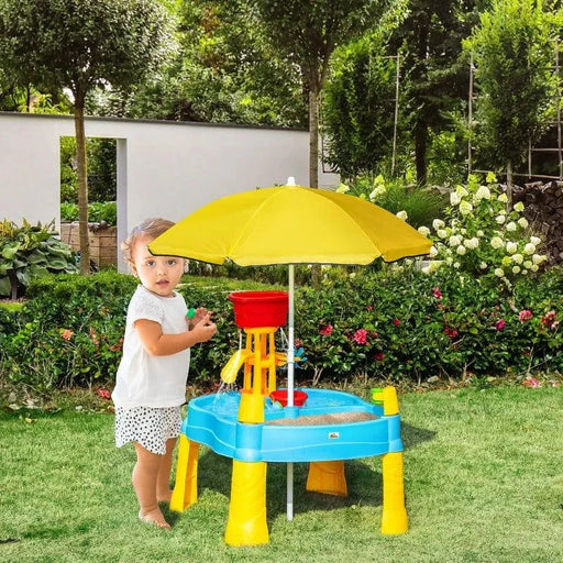 Toddler playing at blue 2-in-1 sand and water activity table with yellow umbrella in garden.