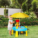 Toddler playing at blue 2-in-1 sand and water activity table with yellow umbrella in garden.