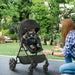 Woman adjusting a black stroller with a child inside in a garden setting