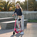Woman with glasses on a pink electric scooter with seat outdoors near concrete benches