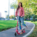 Woman riding pink 24V electric scooter with adjustable seat on park path, foldable design