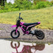 Pink 24V kids electric dirt bike with black details on gravel next to grass and puddle