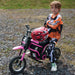 Child in motocross gear next to pink 24V kids electric dirt bike with helmet outdoors