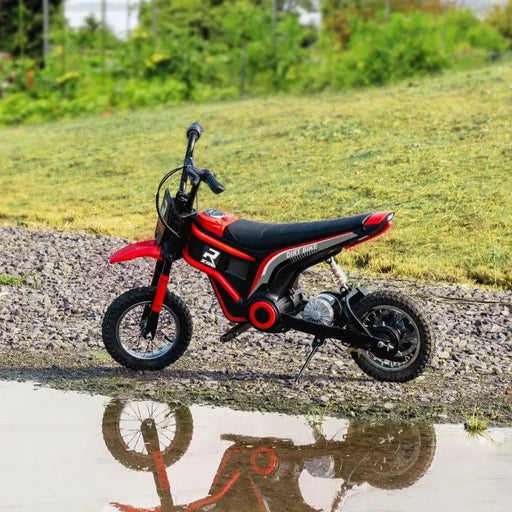 Red 24V kids electric dirt bike on gravel with grass background and water reflection