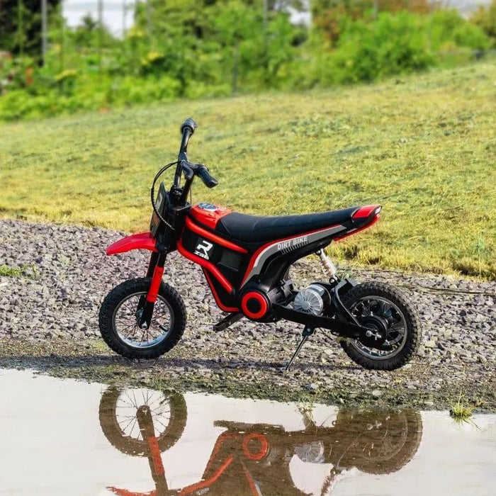 Red 24V kids electric dirt bike on gravel with grass background and water reflection