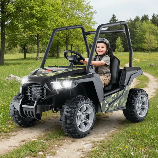 Happy child riding camouflage electric kids’ off-road car with headlights on in grassy park
