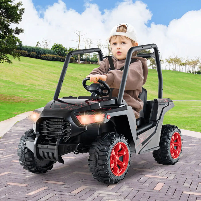 Young child driving black kids ride-on car with red wheels on paved path in park