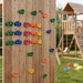 Wooden outdoor kids' climbing wall with colorful handholds and rope near playground set with swings