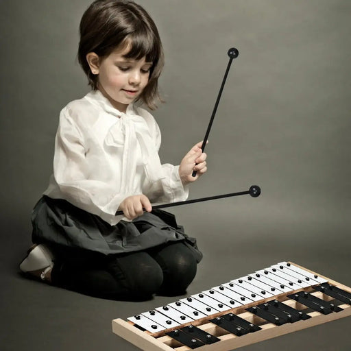 Young girl in white blouse and black skirt playing 27-note glockenspiel with mallets on gray background