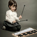 Young girl in white blouse and black skirt playing 27-note glockenspiel with mallets on gray background