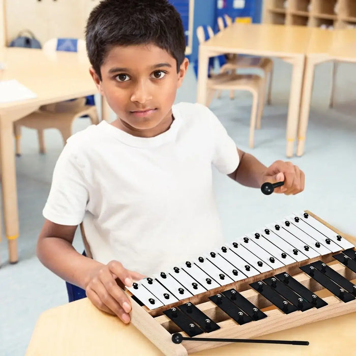 Young boy playing a 27-note glockenspiel xylophone with black and white metal bars in a classroom